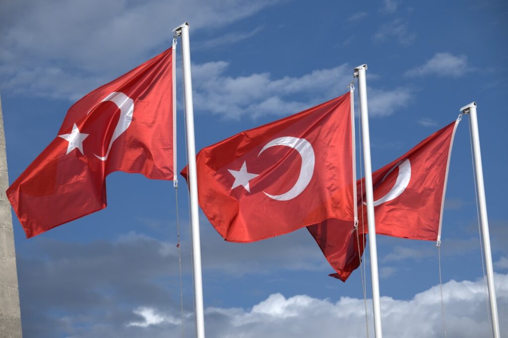 Three turkish flags waving against a cloudy sky.