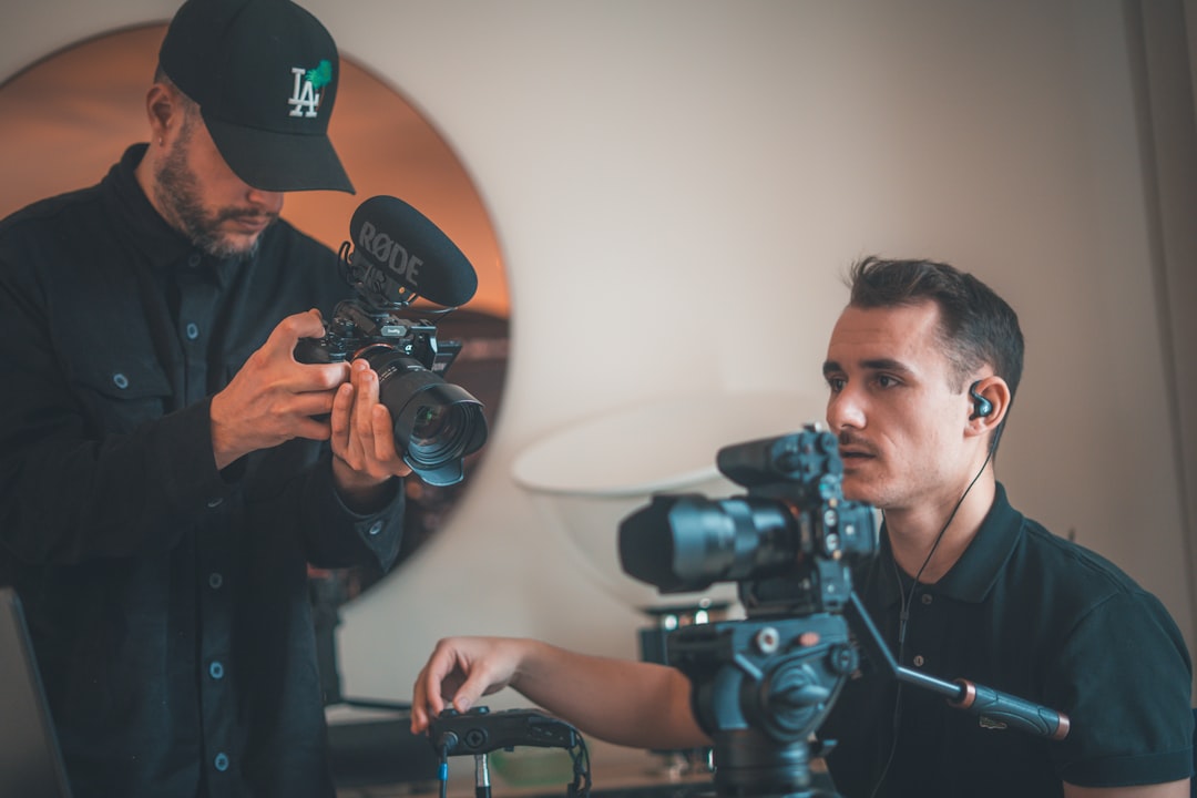 Two men operating professional video cameras indoors.