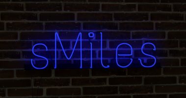 a blue neon sign that says smiles on a brick wall